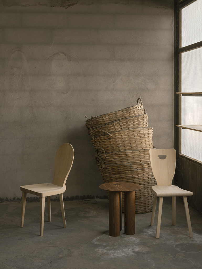 Bord Hommage tillsammans med stolarna Skedblad och Sörgården, bägge med design av Carl Malmsten. Står på betonggolv med staplade korgar i bakgrunden.