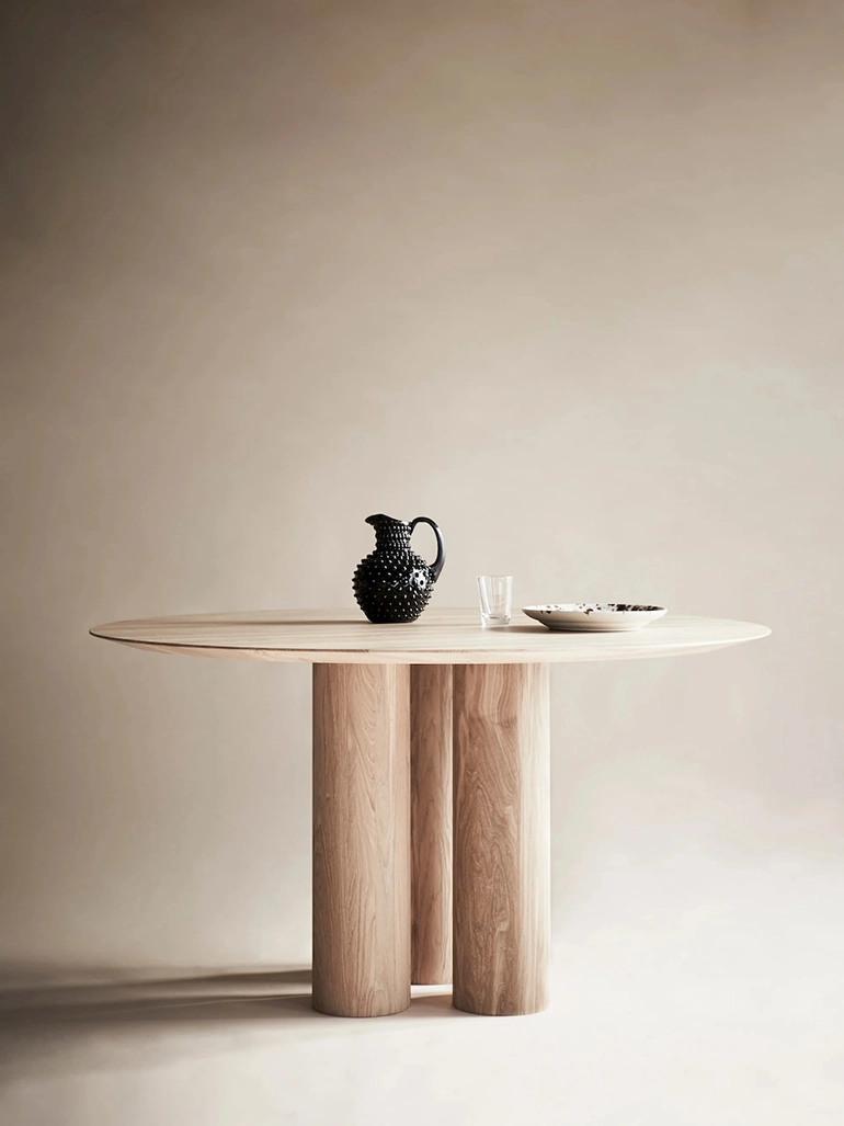 runt matbord i ljust trä, keramiktallrik, ett glas och en svart kanna står på bordet